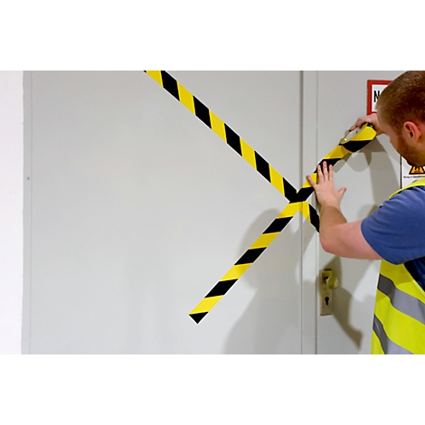 A man applies black and yellow warning tape to a door. The door is closed, and the tape crosses.