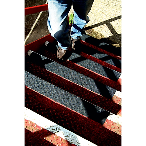 Person standing on metal stairs. The steps are red and black. The person is wearing jeans and brown shoes.