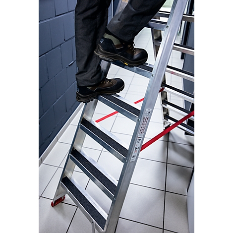 Person is climbing a silver ladder. Black shoes on non-slip steps. Red stripe on the floor.
