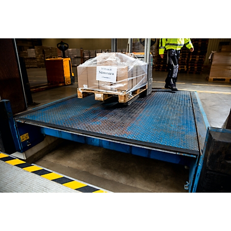 A worker in a yellow jacket loading or unloading boxes on a loading dock.