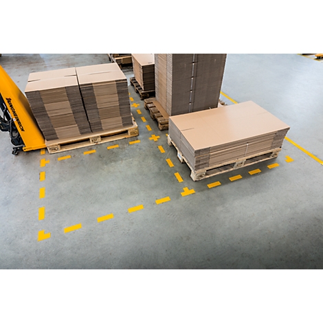 Stacks of cardboard on pallets in a warehouse, yellow markings on the floor.