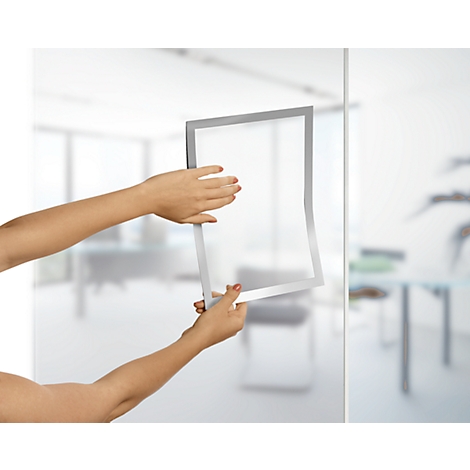 Two hands holding a rectangular, silver-colored frame. The background is blurred, an office.