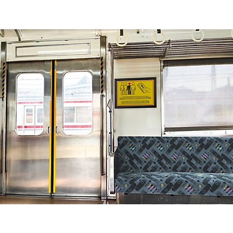Interieur van een trein met zilverkleurige deuren, een gestoffeerde zitting en een geel waarschuwingsbord aan de muur.