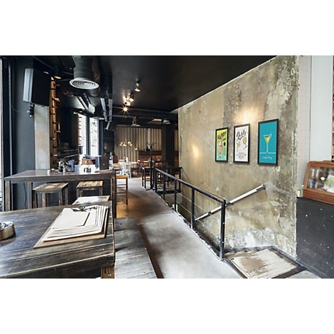 Modern restaurantinterieur met rustieke houten tafels, betonnen muren en drie ingelijste foto's.