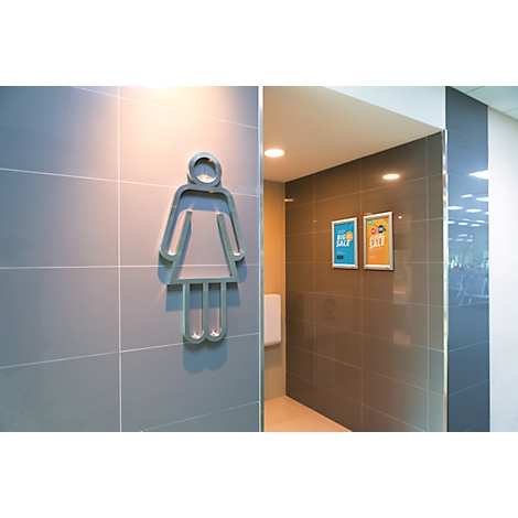 Ein Frauensymbol an einer Wand, die zu einem Toilettenraum führt. Zwei Schilder an der Wand.
