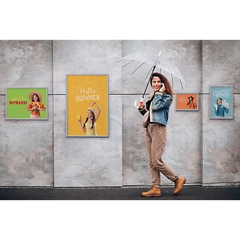 Eine Frau mit Regenschirm läuft vor einer grauen Wand, an der saisonale Poster für Frühling, Sommer, Herbst und Winter hängen.