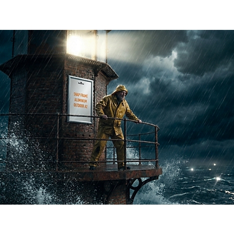 Ein Leuchtturmwärter im Regen steht neben einem Aluminium-Klapprahmen an einem stürmischen Leuchtturm.