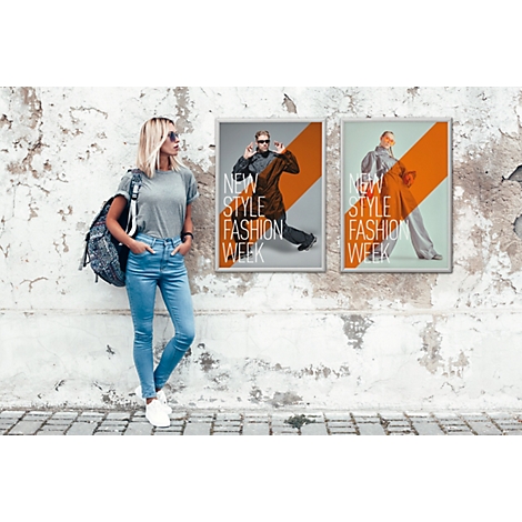 Eine Frau mit Rucksack lehnt an einer Wand mit zwei Werbeplakaten für eine Fashion Week.