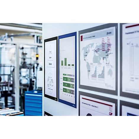 Several framed diagrams and charts on a white wall. A factory in the background.