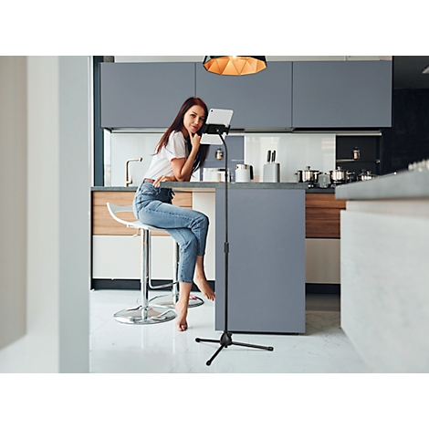 Young woman sitting at kitchen counter. She rests her chin on her hand and looks into the camera. Next to her, a tablet on a tripod.