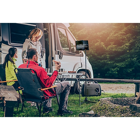A family relaxing in front of a camper. The man is sitting in a chair, the others are standing.