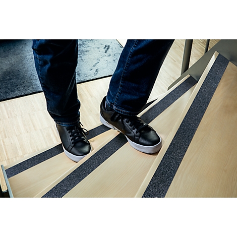 Person walking on wooden stairs. Black shoes, blue jeans. Black non-slip strips on steps.