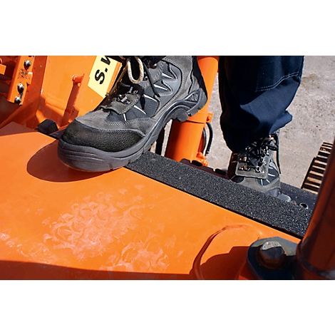Two feet on an orange machine. Black boots stand on a black non-slip surface. The machine says "S.M."
