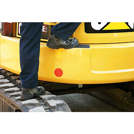 Close-up: worker stepping onto track of yellow excavator. Boots, legwear, detail. Red dot, black stripe.