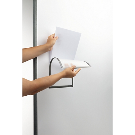 Handen plaatsen papier in een aan de muur gemonteerde houder. De houder is van metaal en hangt aan een witte muur.