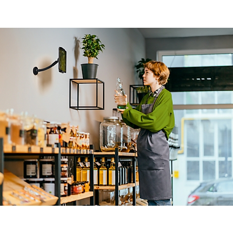 Jonge vrouw houdt glazen fles vast in duurzame winkel, draagt een schort.