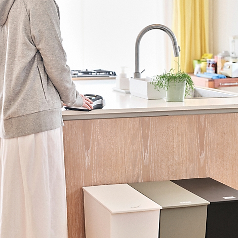 Persoon staat in een lichte keuken naast drie moderne prullenbakken in verschillende kleuren.