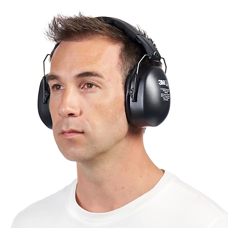 A man wearing black earmuffs on a white background. He wears a white t-shirt and looks to the side.