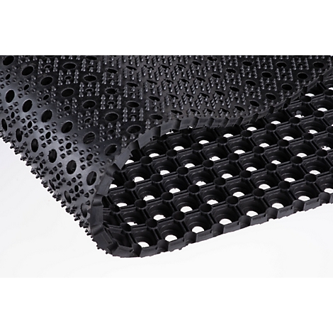 Primer plano de un felpudo de goma negro con orificios y textura de tachuelas.