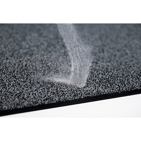 Primer plano de una alfombra gris texturizada con polvo blanco o fibras depositándose en forma de remolino.