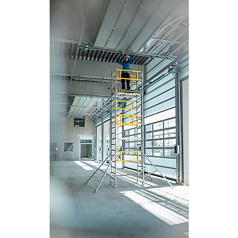 Personne travaillant sur le plafond sur un échafaudage. Chantier avec porte roulante ouverte.