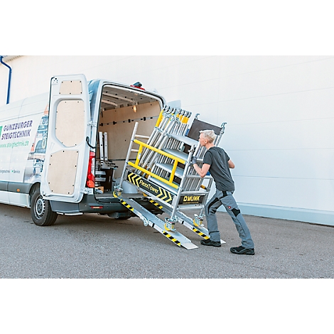Un homme pousse un échafaudage hors d'une camionnette. Bandes d'avertissement jaunes et noires sur la rampe et l'échafaudage. Logo: DÜNZBURGER STEIGTECHNIK.