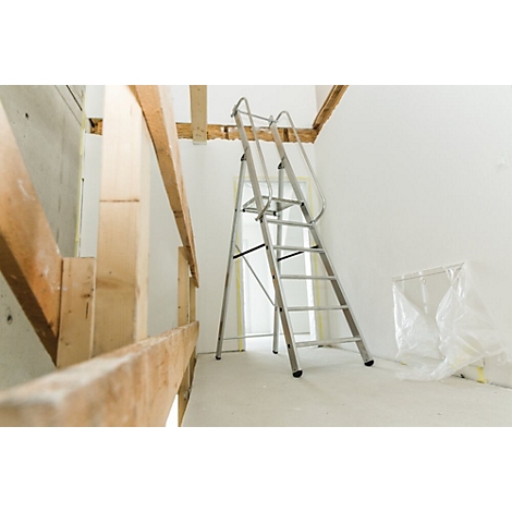 Un escabeau se trouve dans une pièce en construction. Construction en bois au premier plan, fond blanc. Porte et feuille de plastique en arrière-plan.