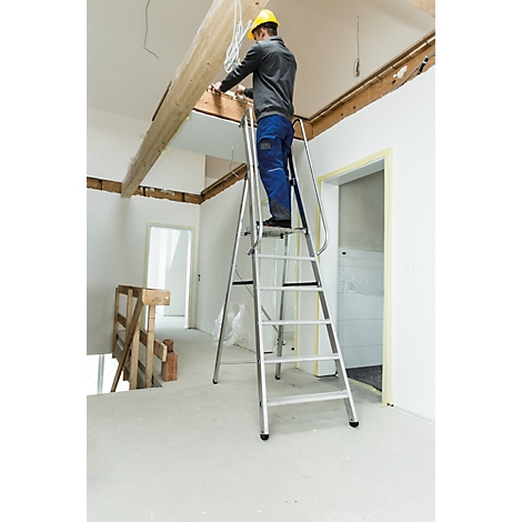Un homme sur une échelle travaille sur une construction de plafond. Il porte un casque jaune et des vêtements de travail.