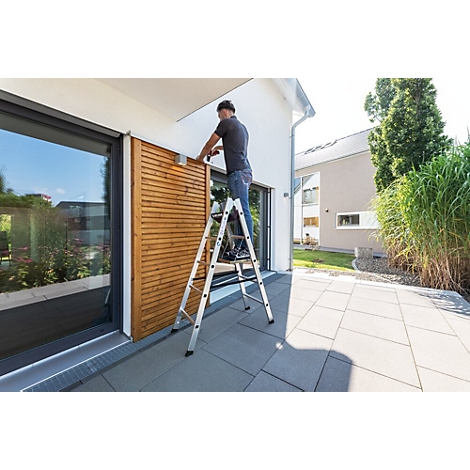 Un homme sur une échelle fixe un revêtement en bois sur un mur de maison.