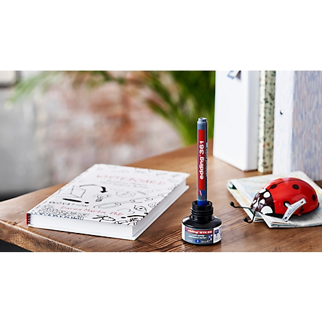 Pen in inktpot, boek met tekeningen, lieveheersbeestjesdecoratie op bureau.