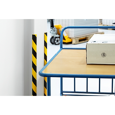 A package rests on a trolley. Yellow and black markings on pillars. Forklift in the background.