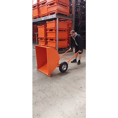 Ein Mann zieht eine orangefarbene Schubkarre in einem Lager, vor orangen Boxen.