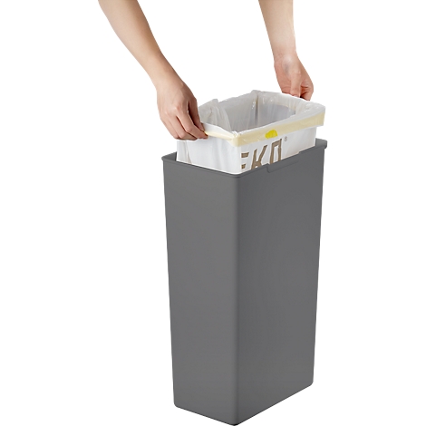 Person hält Müllsack in graue Mülltonne. Der obere Rand des Sacks mit "EKO" Aufdruck ist sichtbar.