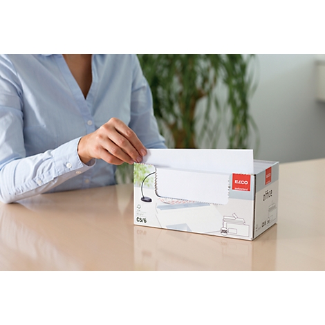 A person pulls a white sheet of paper from a box. The box is labeled "Office". On a table.