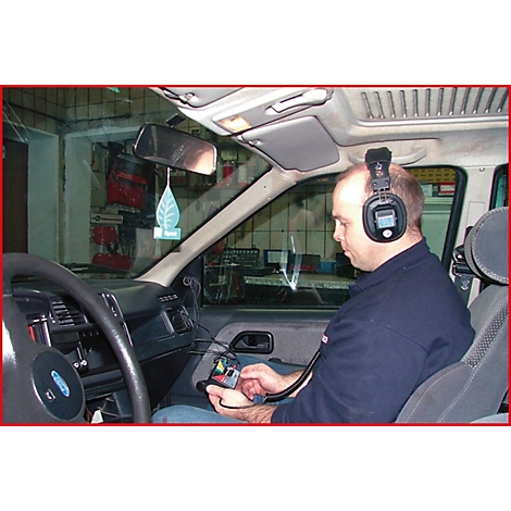 Ein Mann sitzt im Auto mit Kopfhörern und Gerät in der Hand. Vermutlich Fahrzeugdiagnostik.