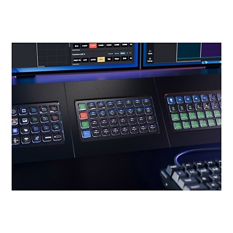 Detaillierte Ansicht einer Live-Produktionskonsole mit leuchtenden Tasten und Bildschirmen. Die Konsole hat verschiedene Bedienelemente für Kameras, Übergänge und andere Effekte.