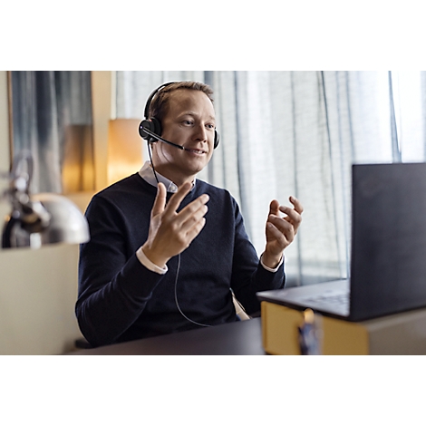 A man with a headset sits in front of a laptop, gesturing with his hands during a video call.
