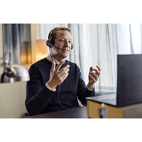 A man wearing a headset gestures with his hands in front of a laptop.