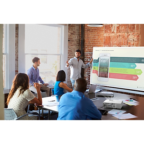 A man giving a presentation in front of a panel, with a smartphone on a screen.