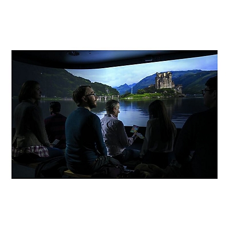 Gruppe betrachtet Projektion einer Burg an einem See. Einige halten Karten. Der Raum ist verdunkelt.