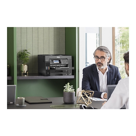 Ein Büro-Setting: Ein Mann mit Brille, im Gespräch mit einem anderen Mann, im Hintergrund ein Drucker.