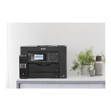 Ein schwarzer Epson-Multifunktionsdrucker steht auf einem weißen Schreibtisch. Dahinter eine weiße Wand. Auf dem Tisch sind dekorative Elemente wie Pflanzen und Vasen zu sehen.