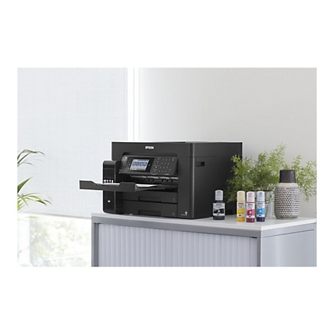 Schwarzer Epson Drucker auf einem weißen Schrank mit Tintenpatronen und Pflanzen; Fenster im Hintergrund.