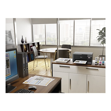 BÃ¼ro, Drucker steht auf Sideboard. Vorne ein Schreibtisch mit Computer, dahinter eine Sitzecke, Fenster im Hintergrund.