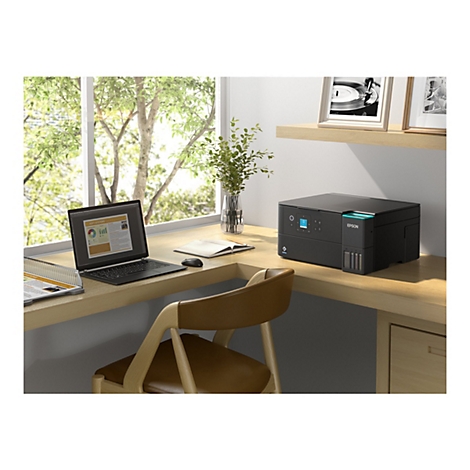 Schreibtisch mit Laptop, Drucker, Vase, Stuhl, Bildern; Büro eingerichtet.