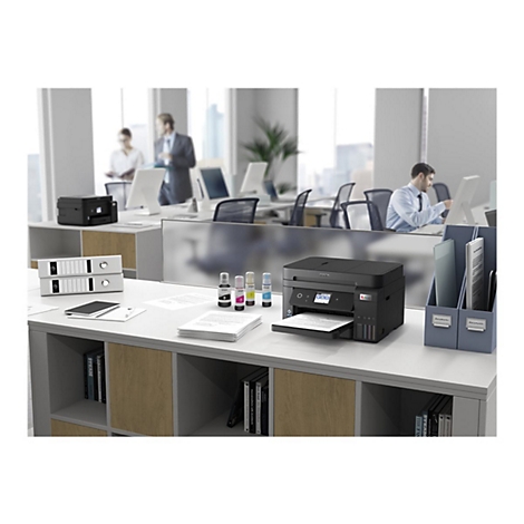 Ein Drucker steht auf einem Schreibtisch in einem BÃ¼ro. Im Hintergrund arbeiten weitere Personen.