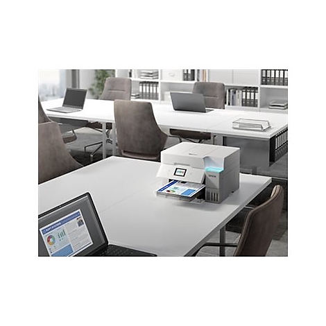 Une imprimante imprime une feuille de papier dans un espace de bureau. Un ordinateur portable est visible au premier plan.