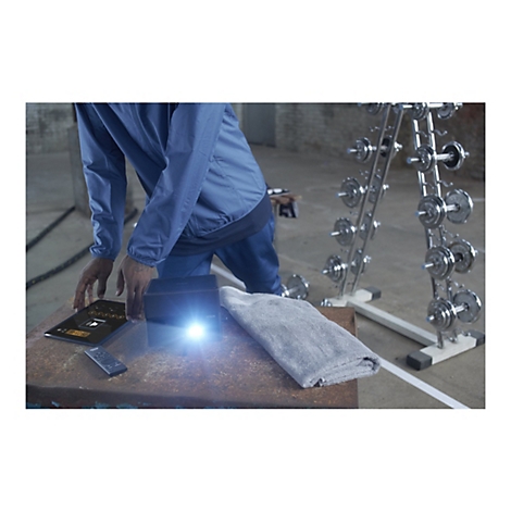 Mann in blauem Anzug bedient Tablet, Projektor leuchtet. Handtuch und Hanteln im Hintergrund.