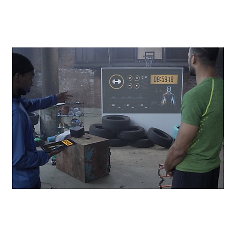 Zwei Männer in einem Fitnessstudio mit einer Anzeigetafel im Hintergrund. Ein Mann zeigt auf ein Tablet.