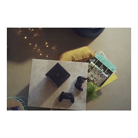 Draufsicht auf einen Tisch mit Projektor, Controllern, Schallplatten und Comics. Warme Lichterkette und ein Kissen im Hintergrund.